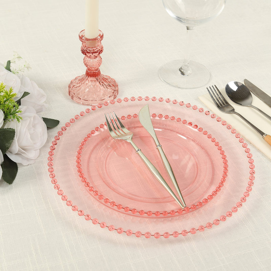 Pink glass plates with silver utensils set on a dining table.