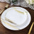 Elegant white dinner plates with gold and black abstract designs on a rustic wooden table.