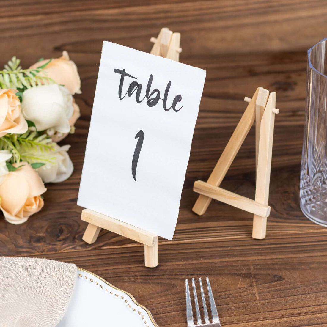 Table number sign on an easel with floral decor and dining setup.