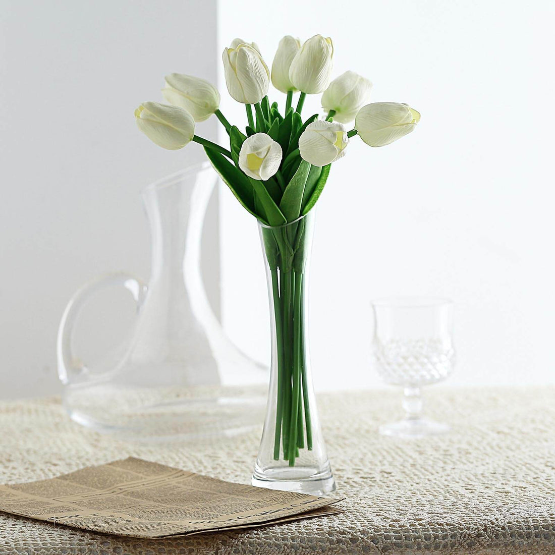White tulip bouquet in a clear vase on a textured surface.