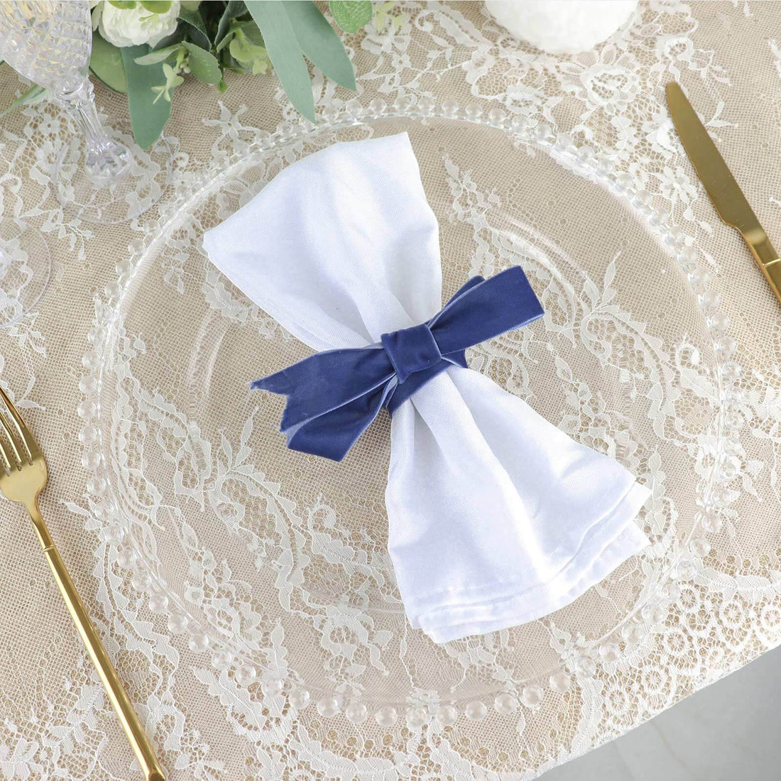Elegant white napkin with navy ribbon on a decorative plate.
