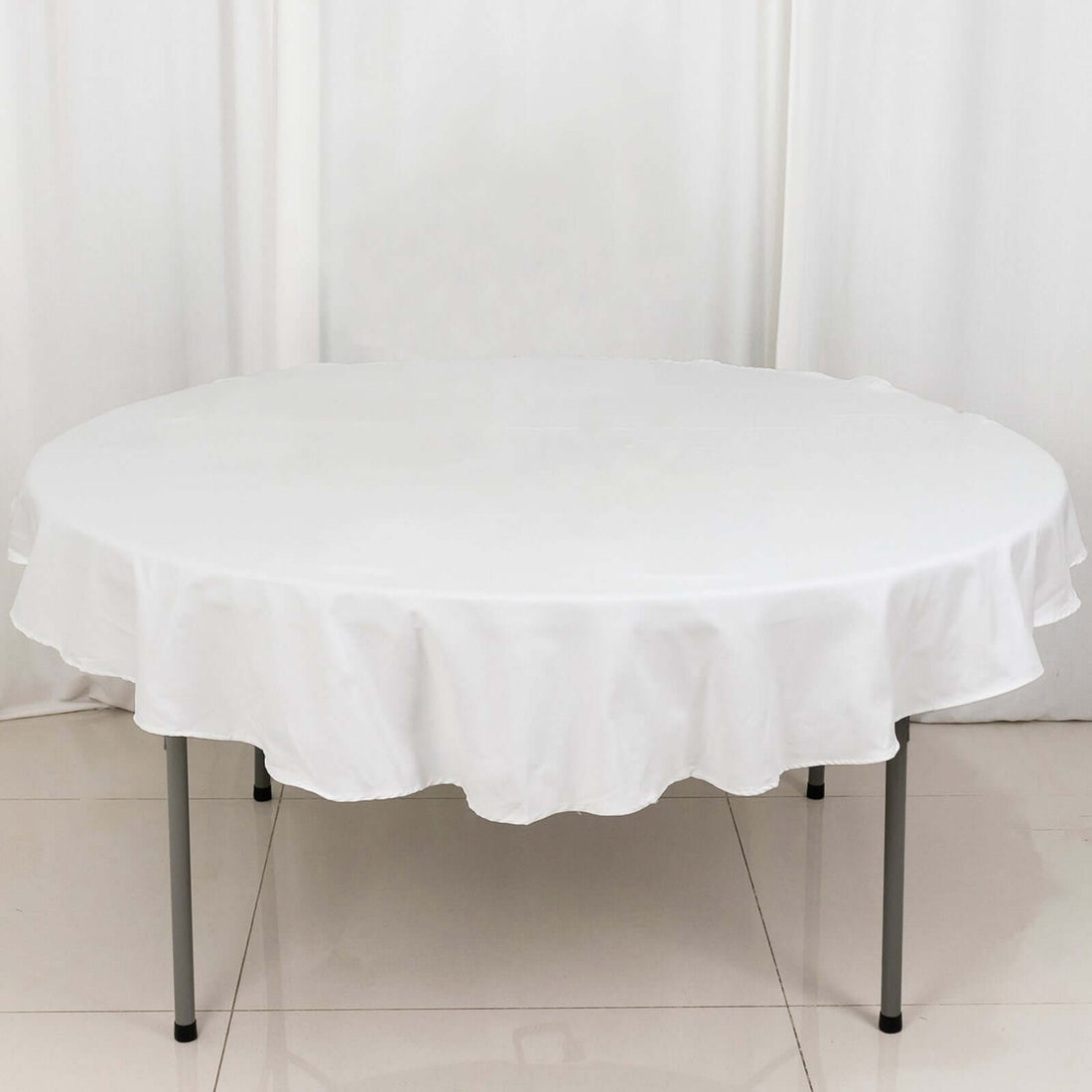 Round table with white tablecloth on a plain backdrop.
