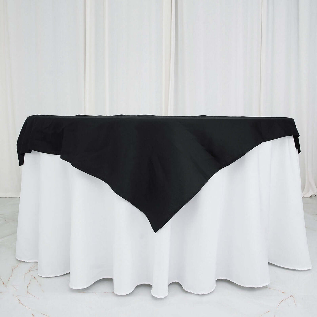 Black tablecloth draped over a white table in a studio setting.