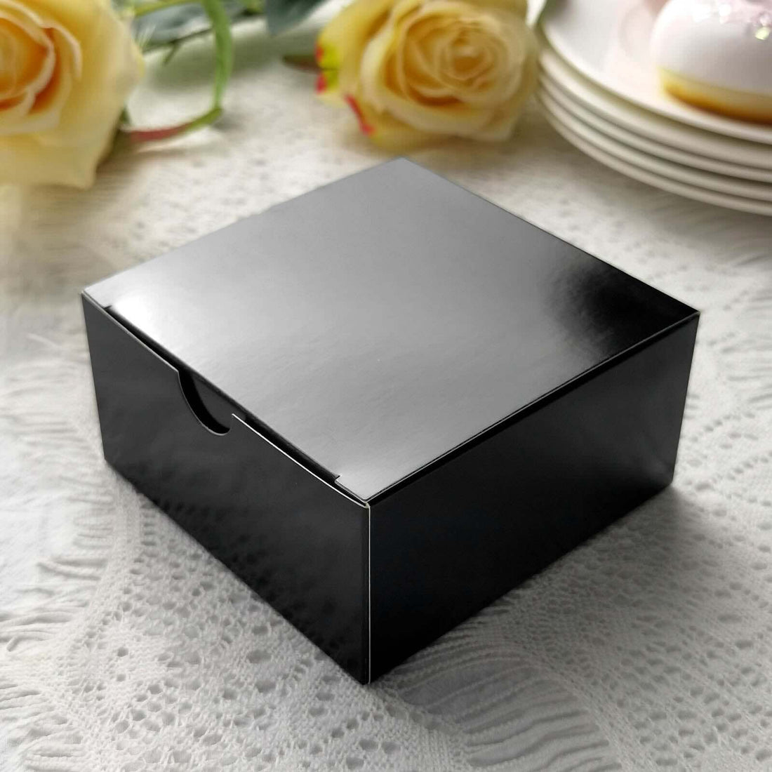 Black gift box with a glossy finish on a textured white lace tablecloth.