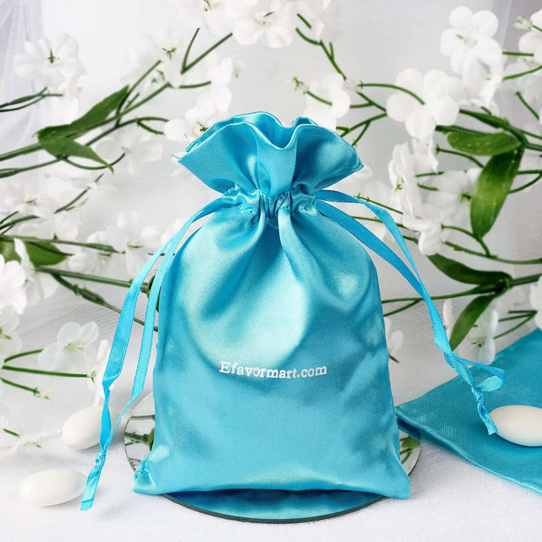 Blue satin drawstring bag with logo on a floral background.