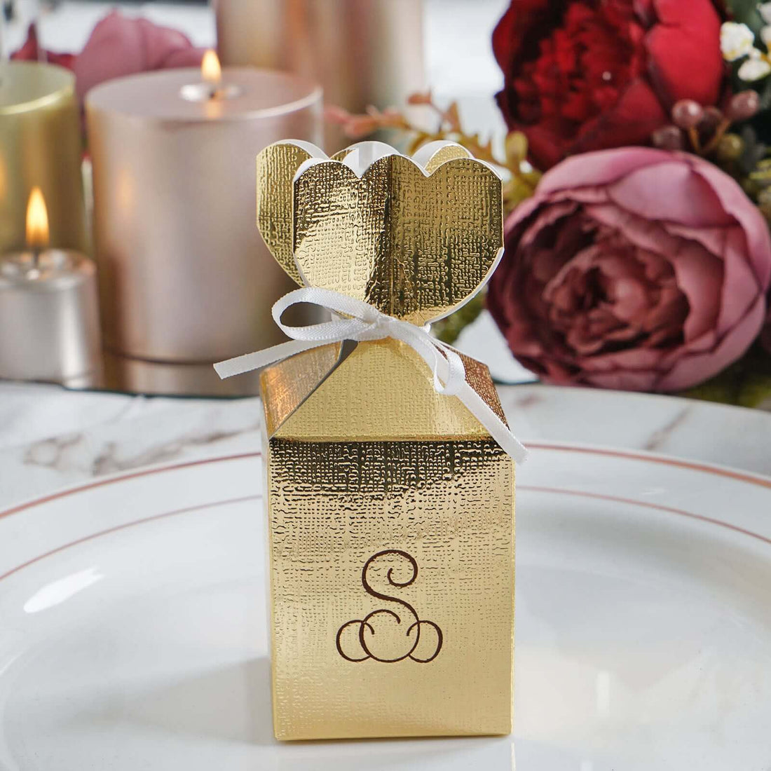 Gold gift box with floral design and ribbon, set on a decorative plate.