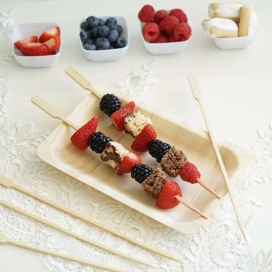 Fruit and granola skewers on a wooden platter with fresh berries in bowls.