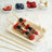 Fruit and granola skewers on a wooden platter with fresh berries in bowls.