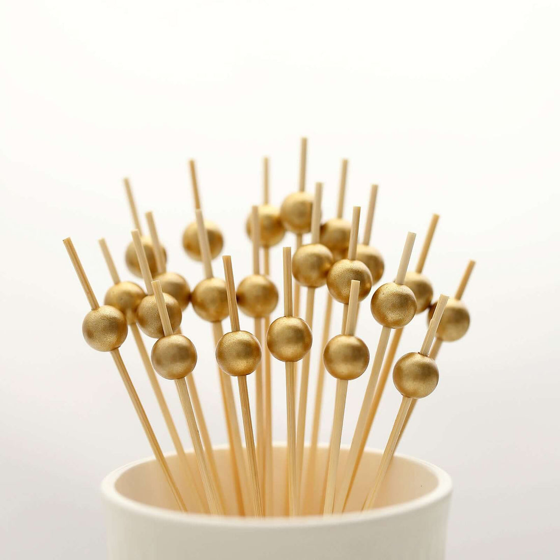 Gold cocktail picks in a cup on a white background.