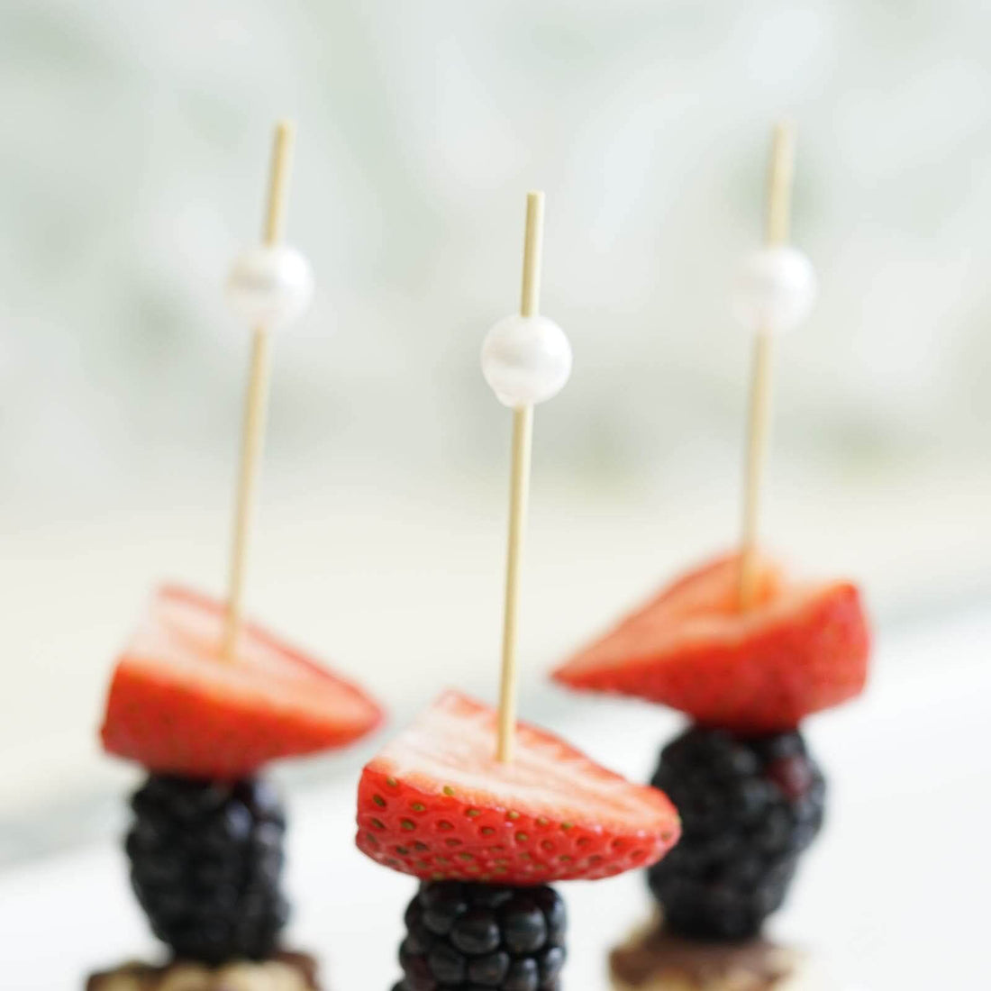Fruit skewers with strawberries and blackberries on wooden sticks.