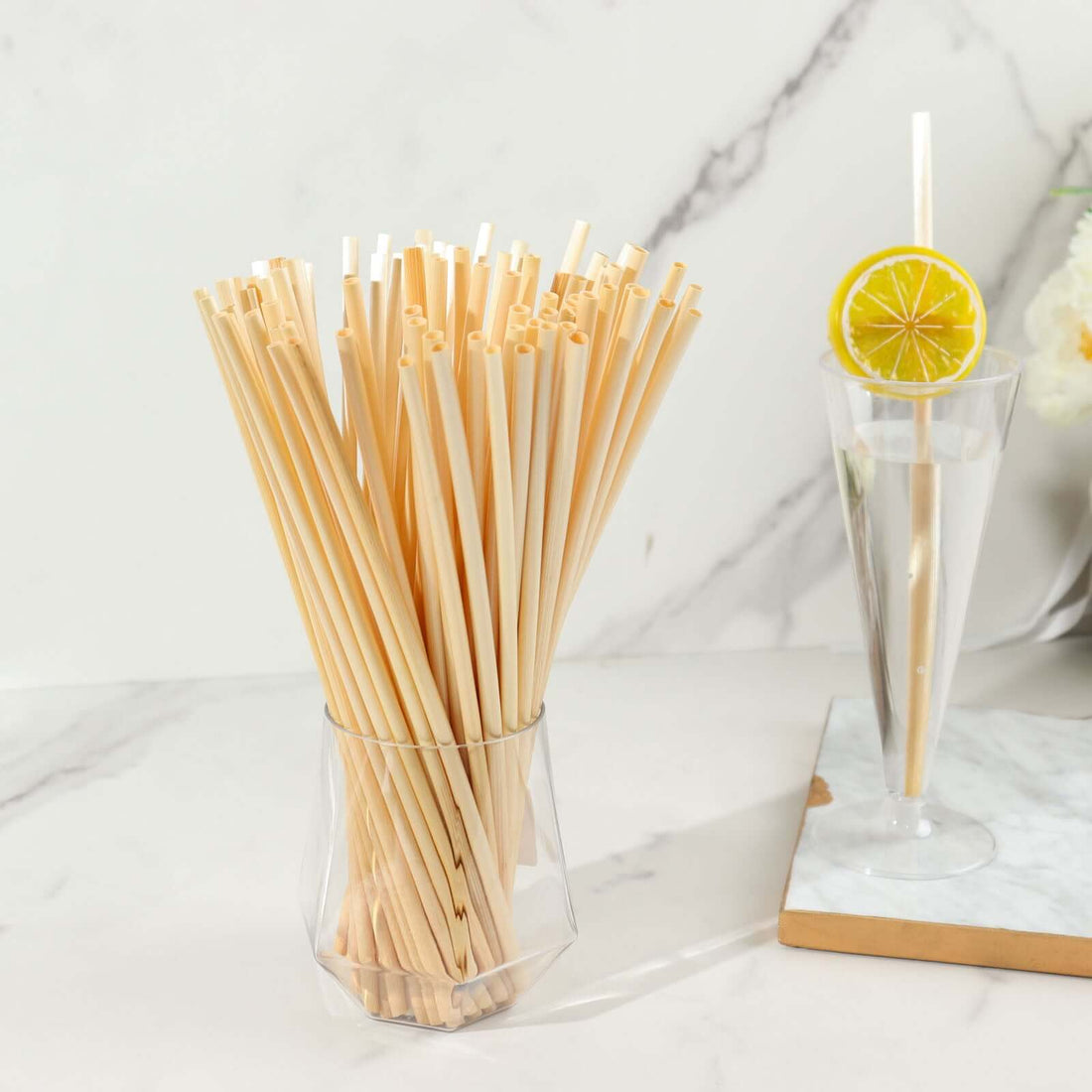 Natural bamboo straws in a clear glass vase on a marble countertop.