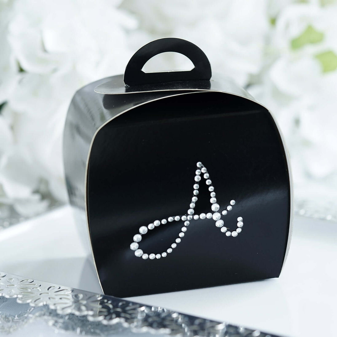 Black gift box with decorative silver letter "A" on a white plate.