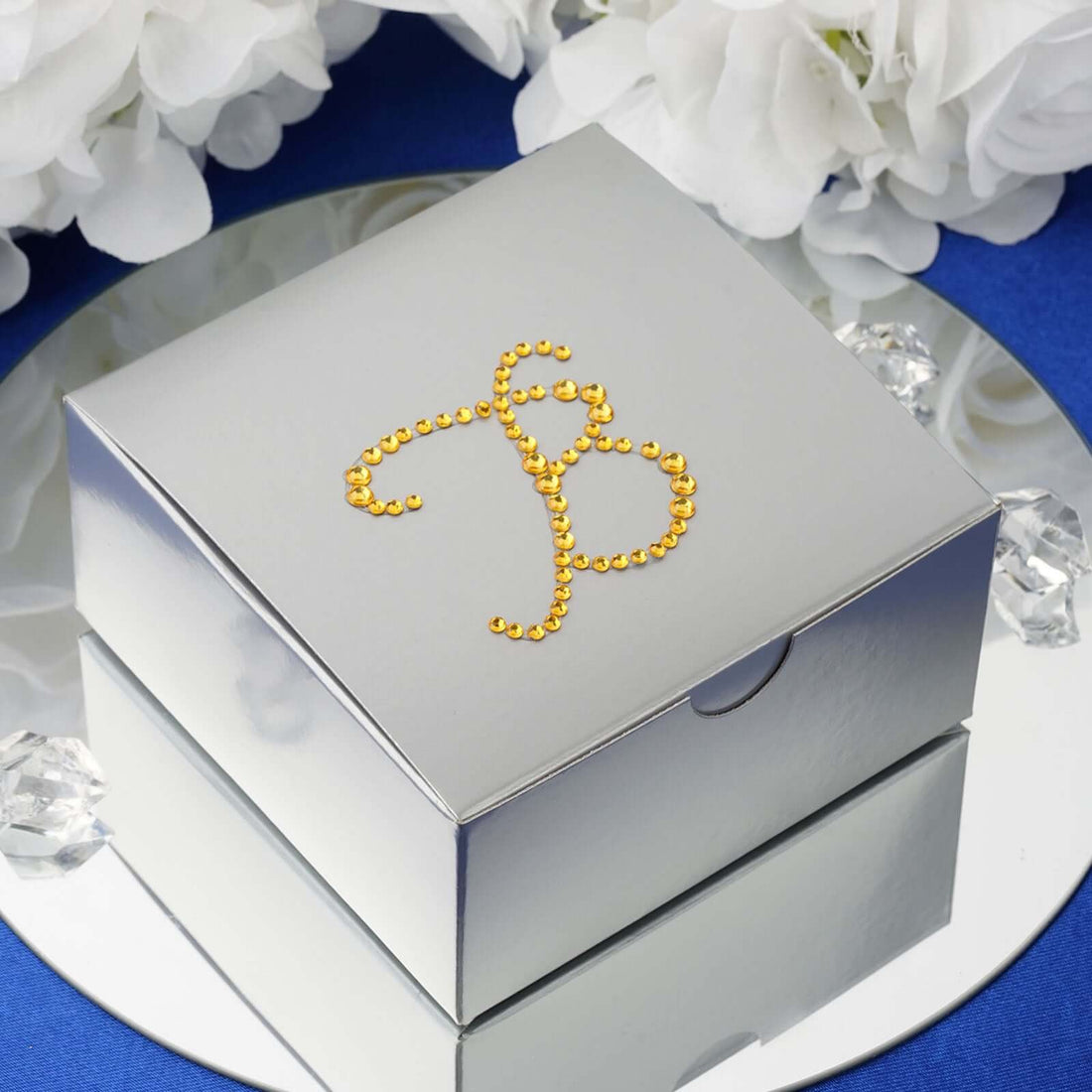 Silver gift box adorned with gold rhinestone design on a reflective surface.