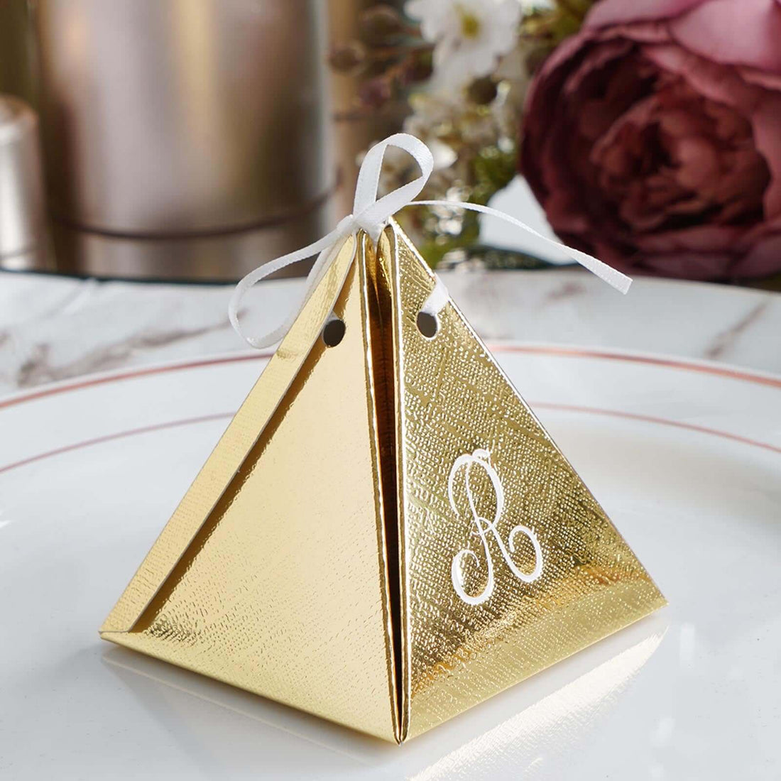 Gold pyramid favor box with a white ribbon and monogrammed letter. #whtbkgd