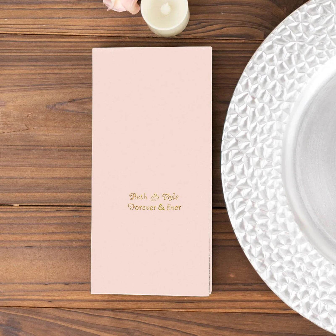 Pink wedding menu with gold text on a wooden table setting.