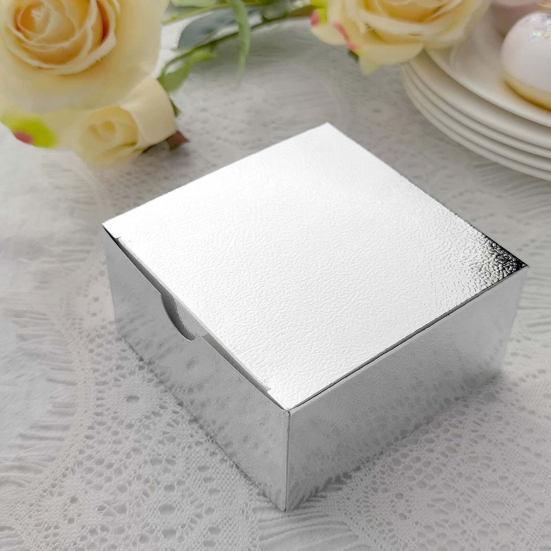 Shiny silver gift box on a textured table setting with flowers.
