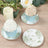 Cupcakes in decorative wrappers with floral plates and a candle on a wooden surface.