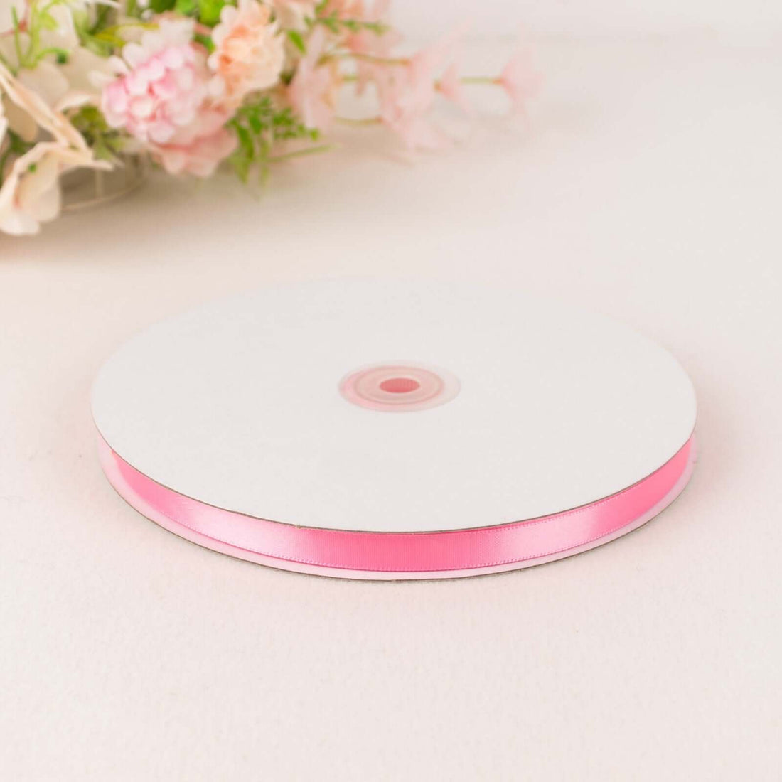 Pink satin ribbon on a spool against a plain background.
