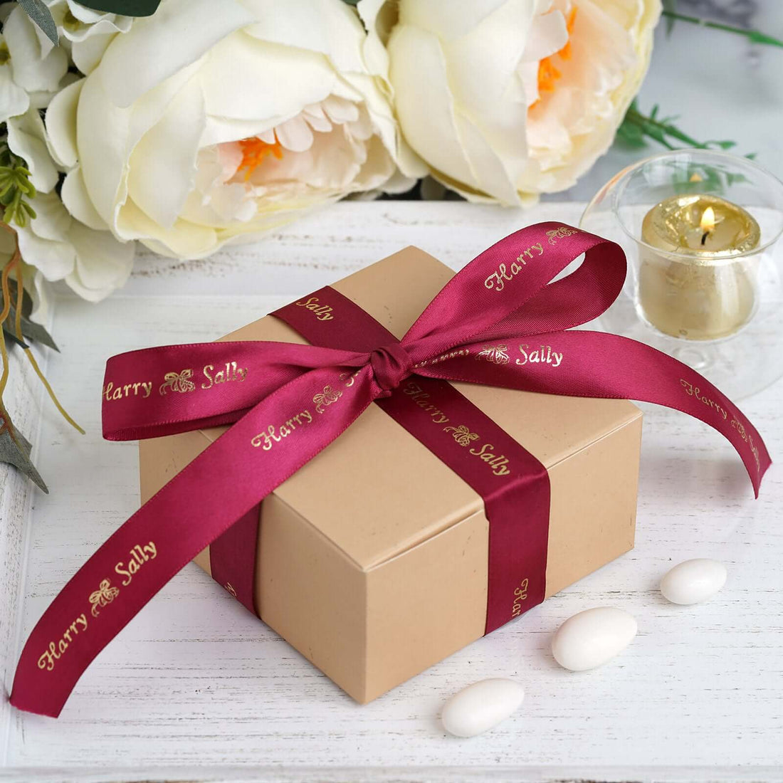 Gift box with burgundy ribbon and personalized text on a wooden table with flowers.