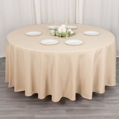 Round beige tablecloth draped over a table set for dining.
