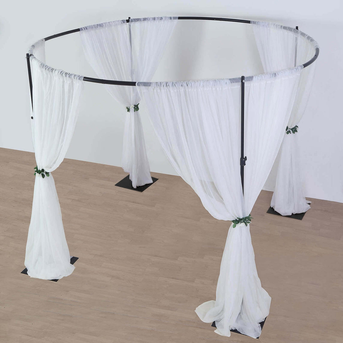 White sheer fabric wedding arch with drapes and green floral accents