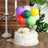 Birthday cake with colorful balloons and decorative flowers on a wooden table.