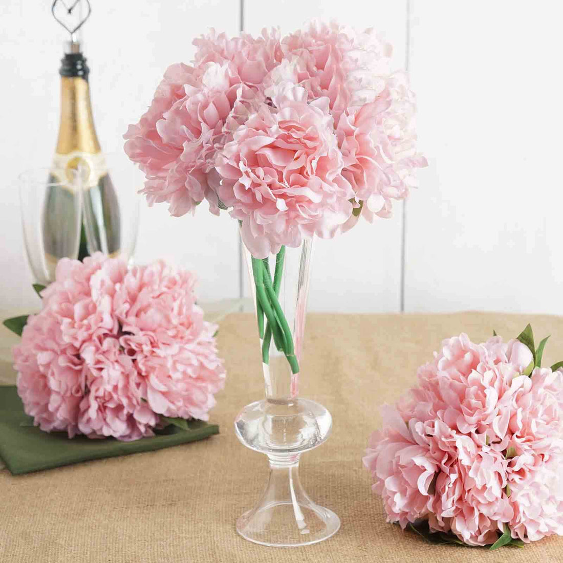 Pink peony bouquet in a glass vase with champagne in the background.