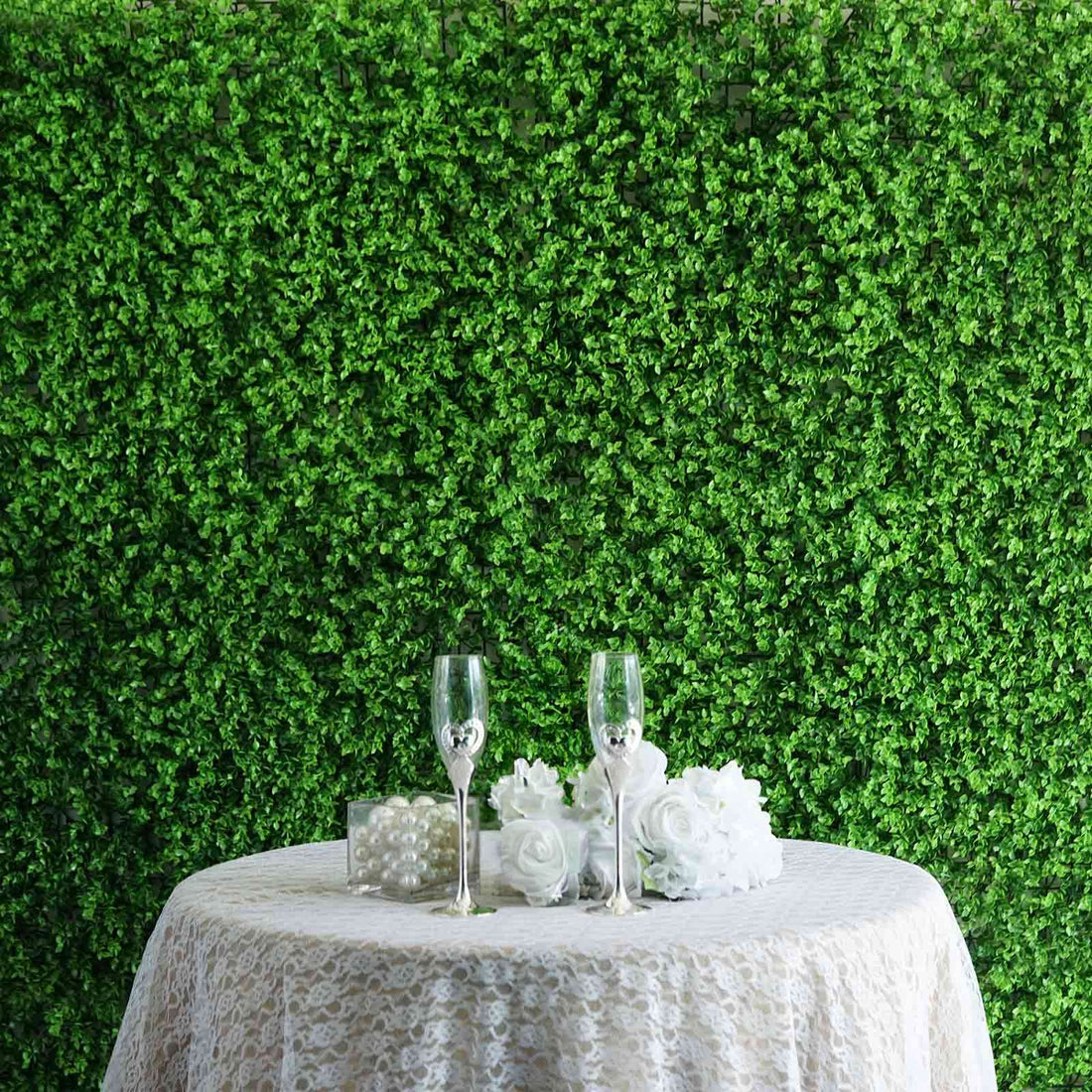 Elegant wedding decor with glasses, roses, and pearls on a lace tablecloth.