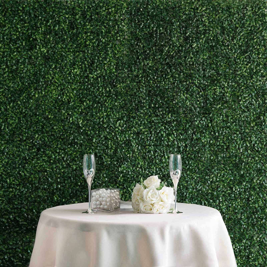 Elegant table setting with champagne flutes and white roses against a green backdrop.