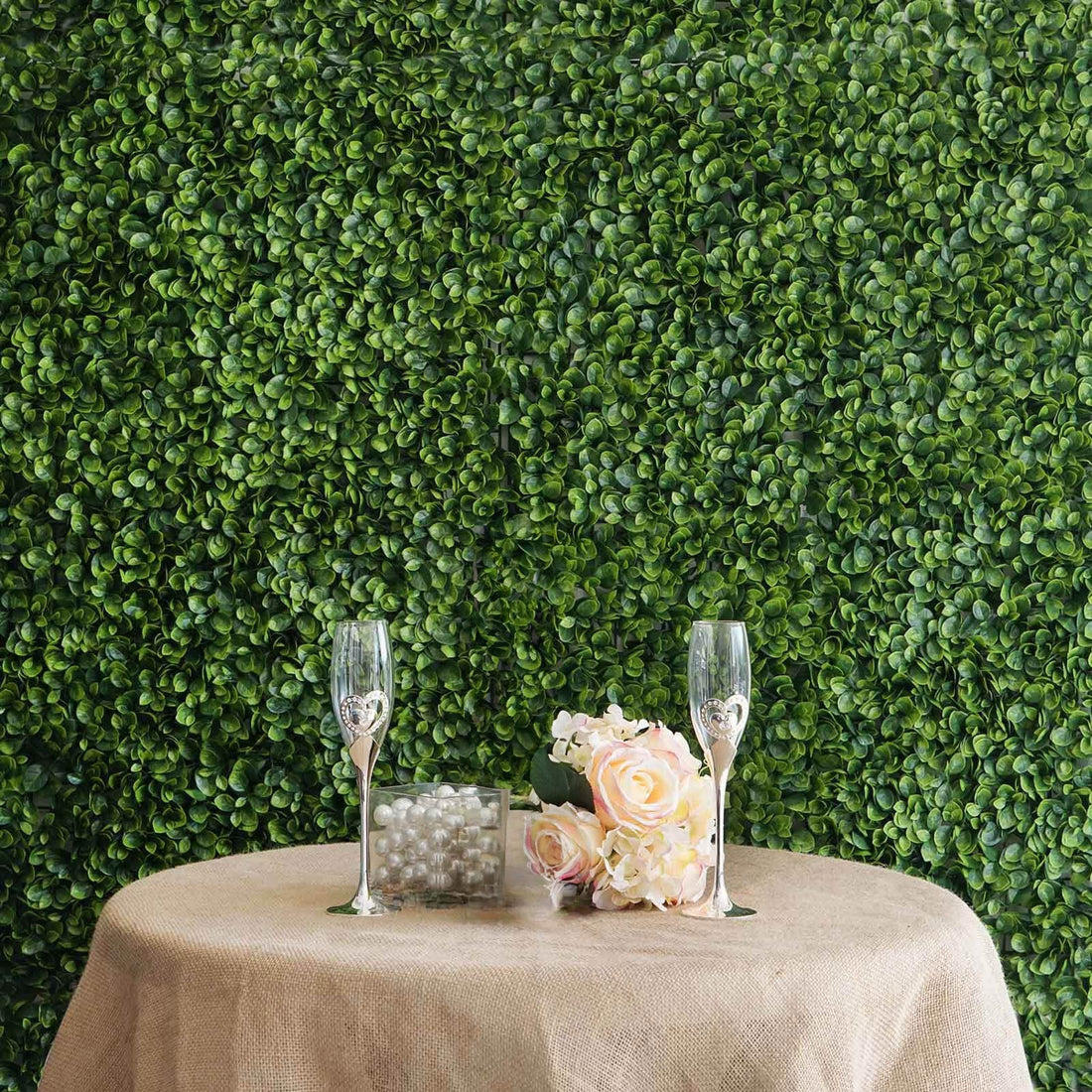 Decorative table setup with glasses and flowers against a green foliage backdrop.