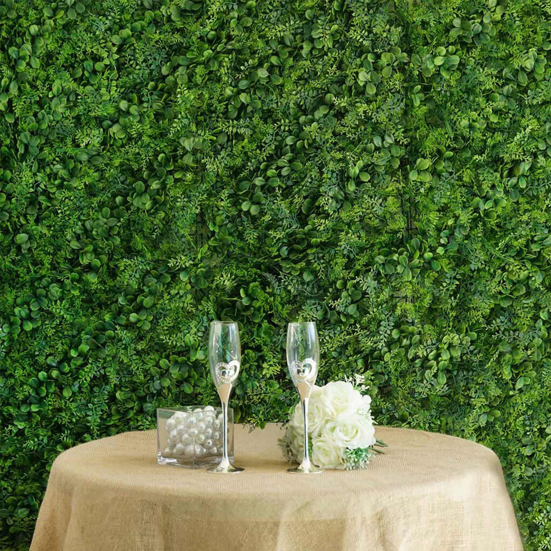 Elegant table setting with champagne glasses, flowers, and greenery backdrop.
