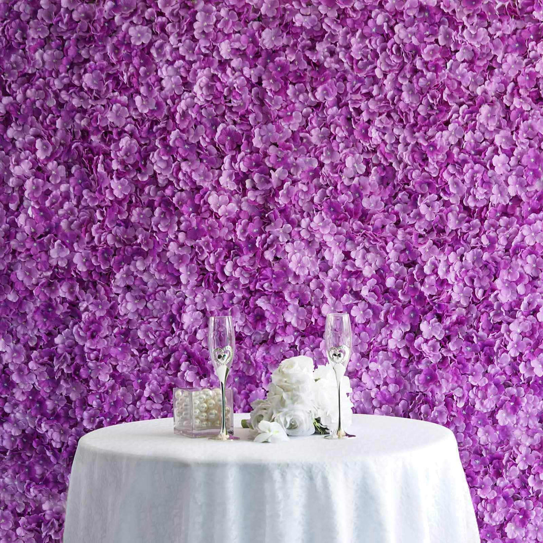 Elegant purple flower backdrop with a table set for two, featuring champagne flutes and decor.
