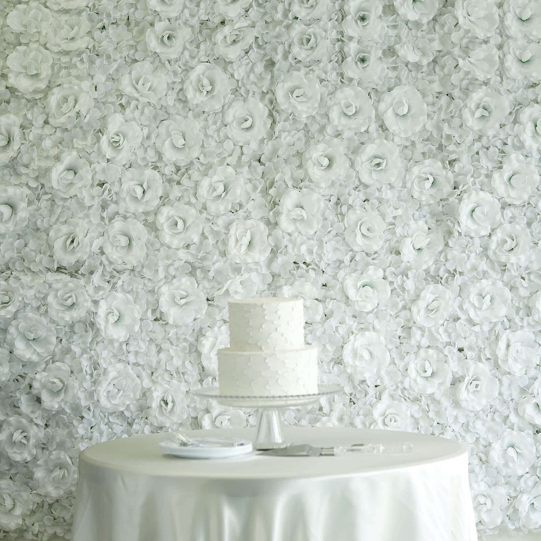 Elegant white wedding cake on a table with a floral backdrop.