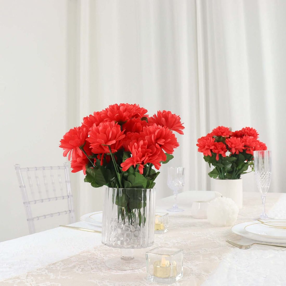 Red daisies in clear vases on an elegantly set dining table.