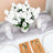 Elegant white rose bouquet centerpiece on a dining table with gold utensils.