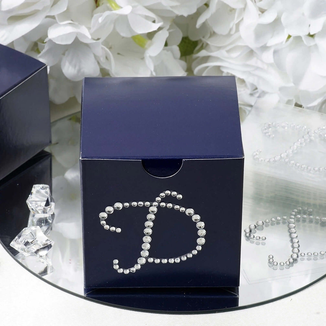 Navy blue gift box with rhinestone "D" design against floral backdrop.