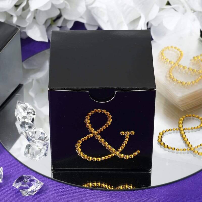Black gift box adorned with yellow rhinestones on a reflective surface.