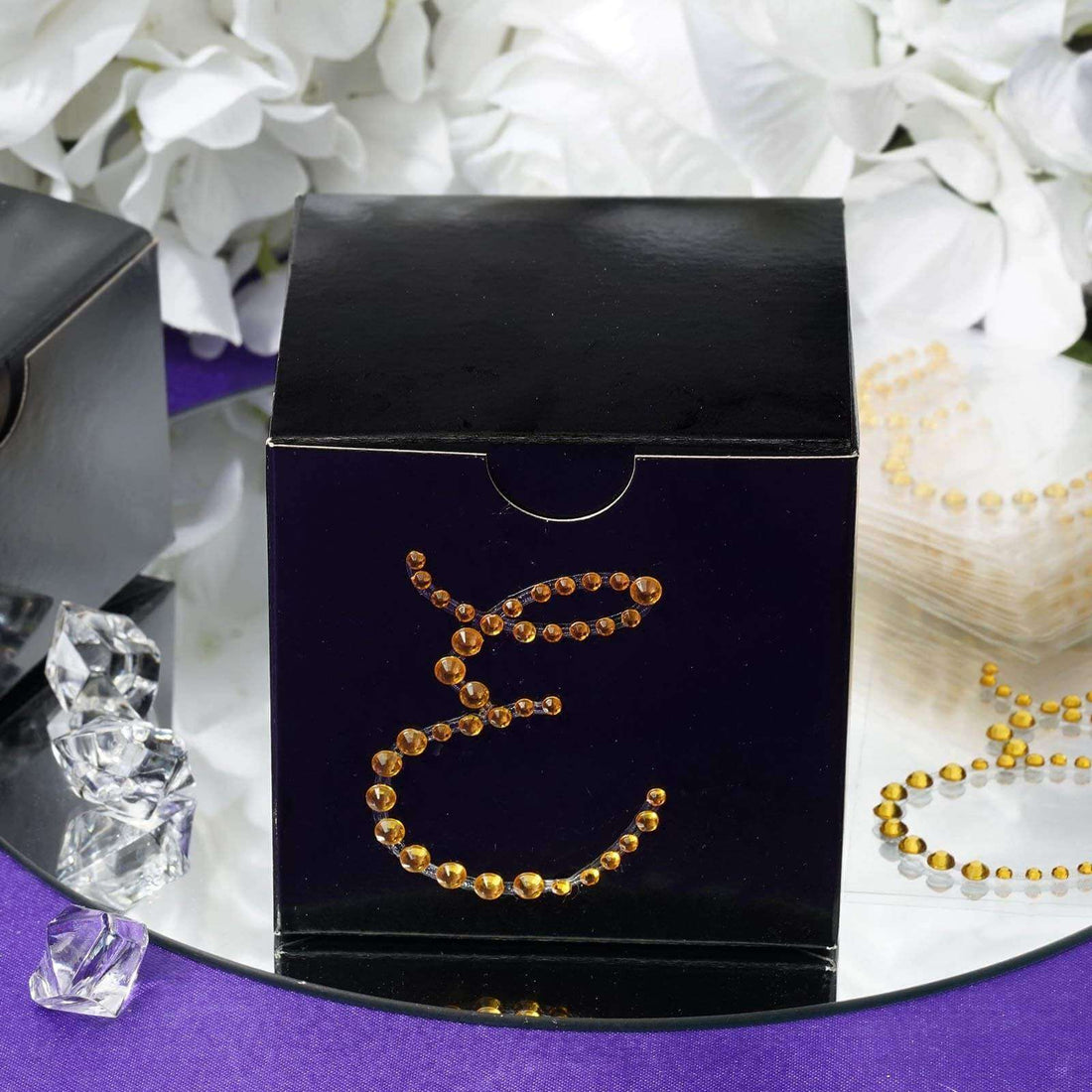 Black gift box adorned with amber gemstones on a reflective surface.