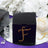 Black gift box with rhinestone 'F' design on a reflective surface.