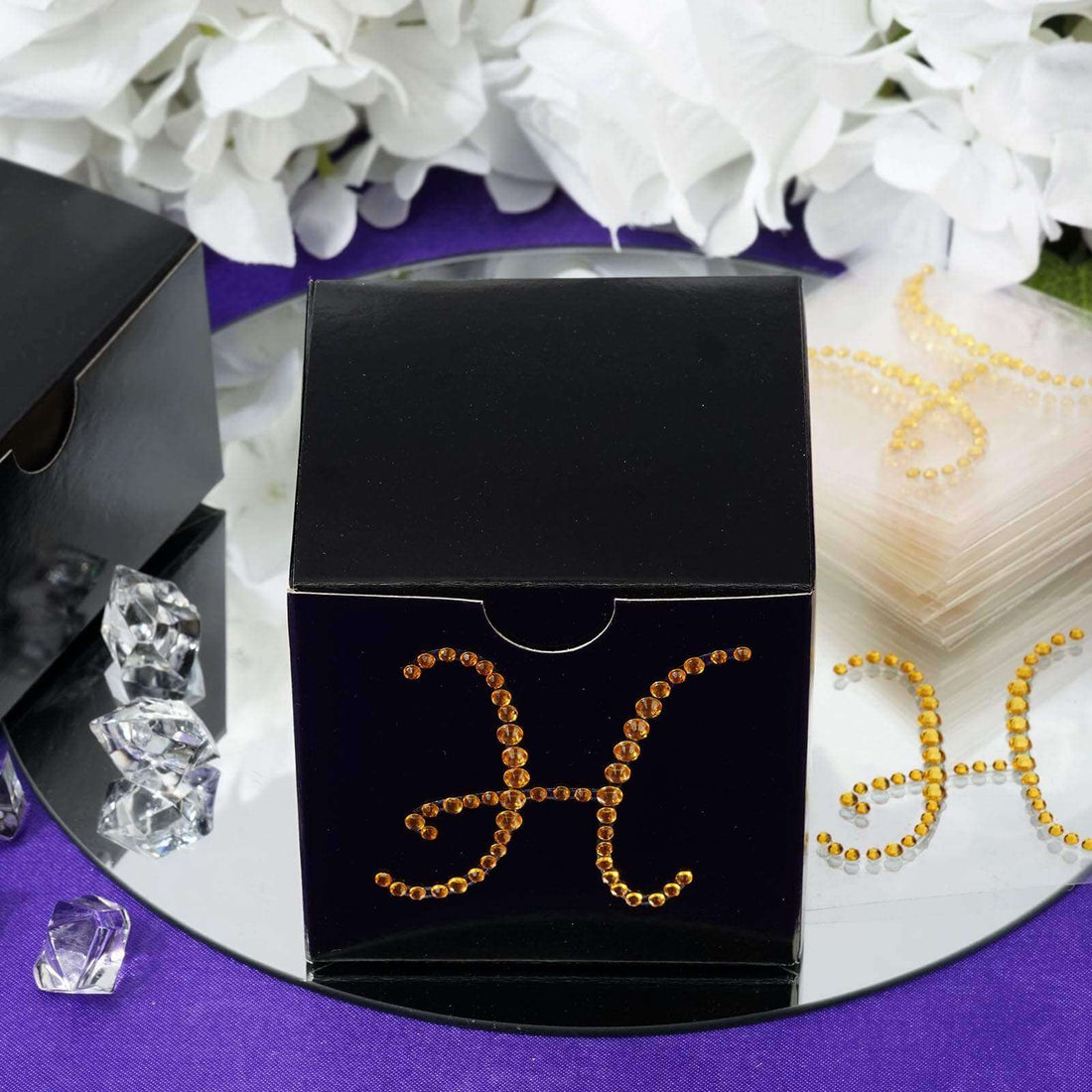 Black gift box adorned with rhinestones on a reflective surface.