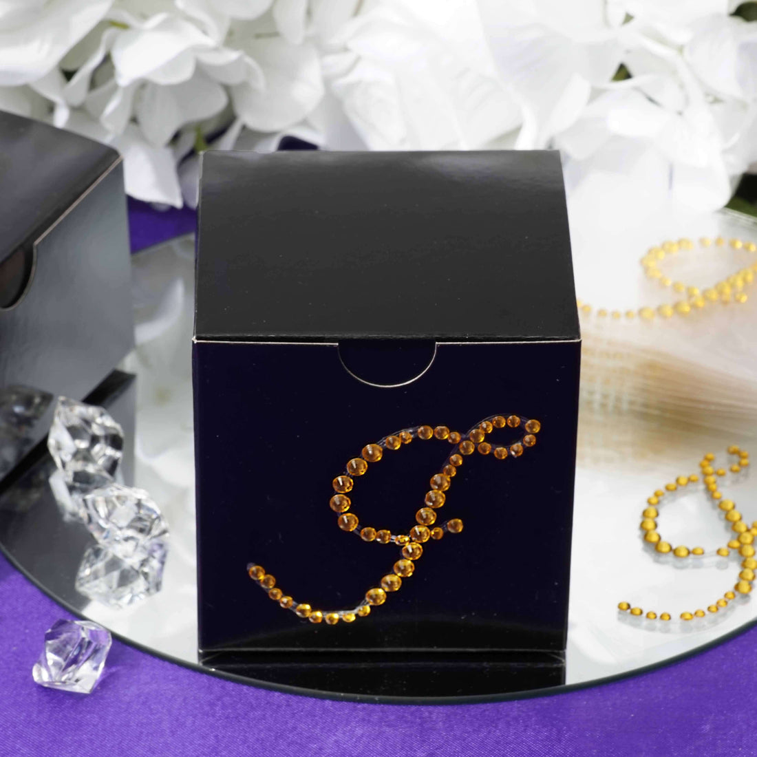 Black gift box adorned with amber rhinestones on a reflective surface.