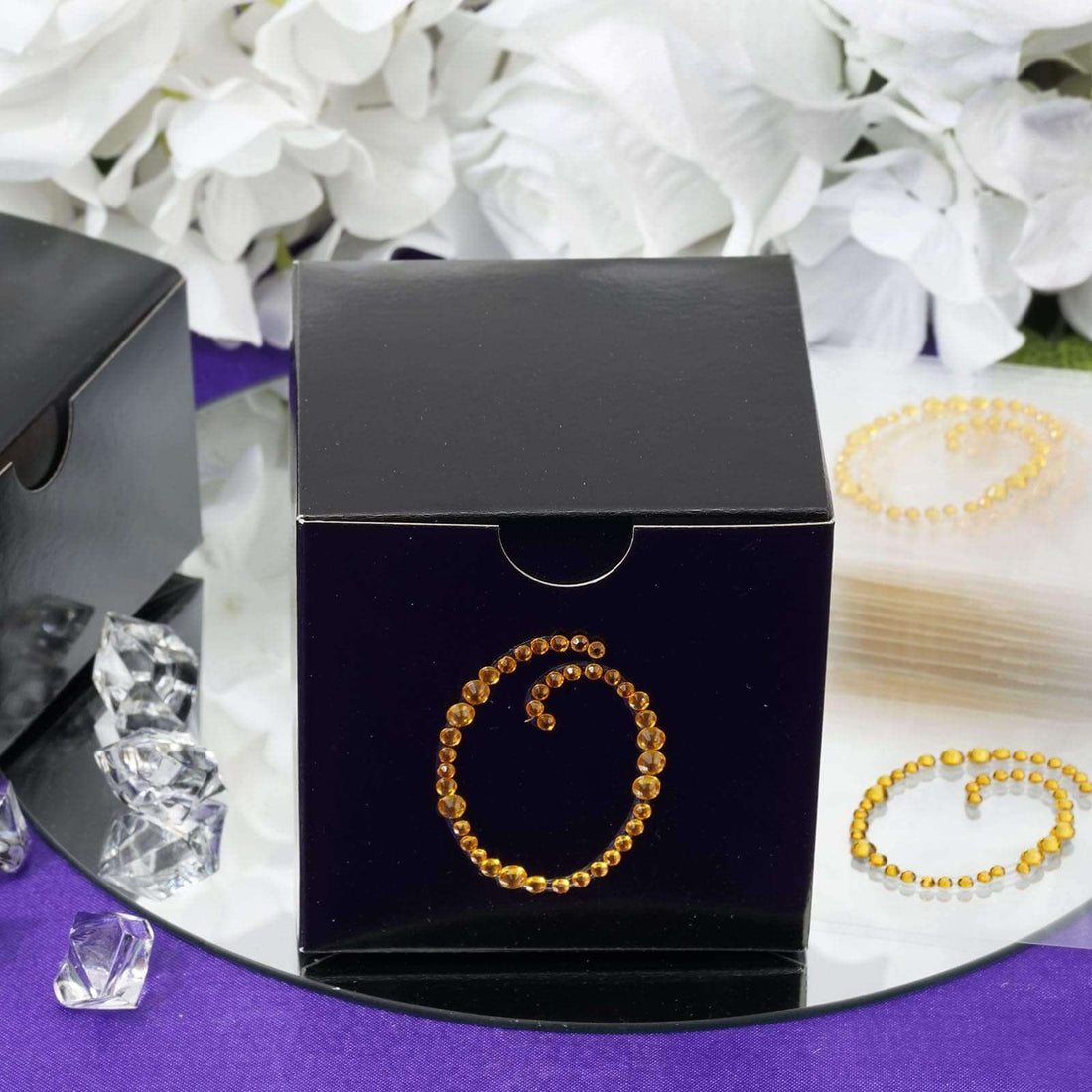 Black gift box with decorative golden swirl design on a reflective surface.