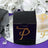 Black gift box with rhinestone letter "P" on a mirrored surface.
