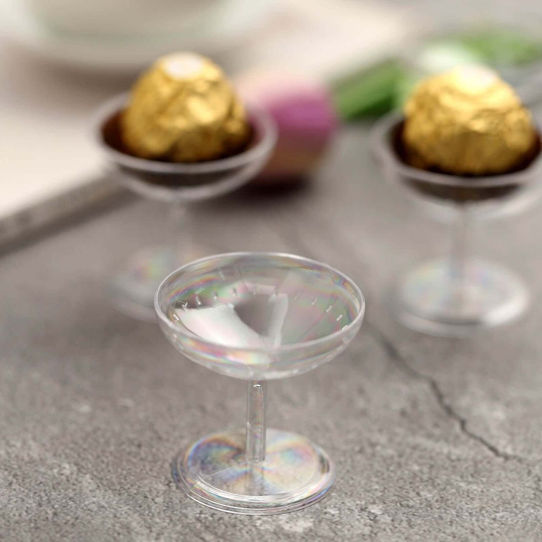 Clear glass dessert cups with iridescent finish on a textured surface.