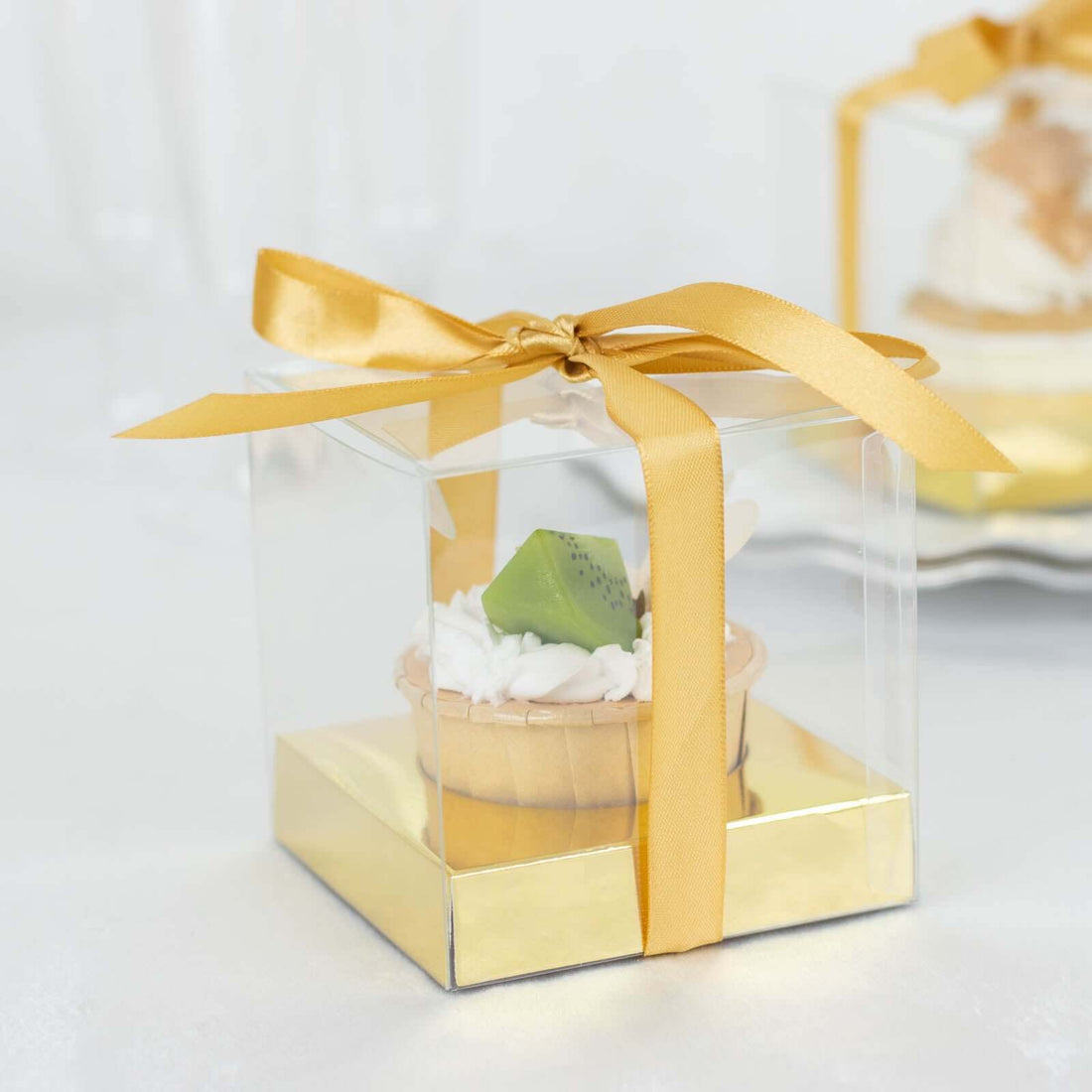 Clear dessert gift box with a golden ribbon and a cupcake inside.