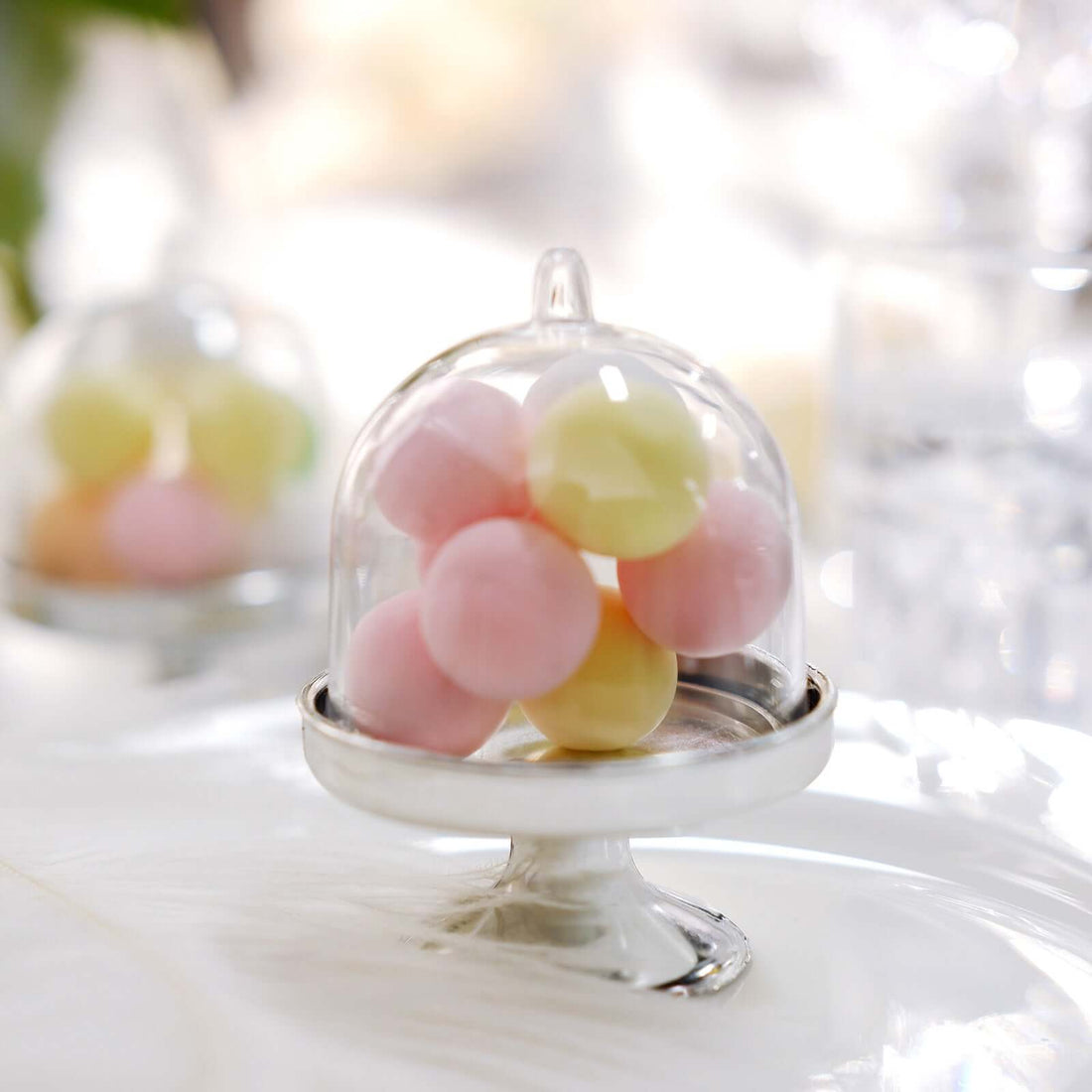 Colorful pastel candies under a glass cloche on a silver stand.