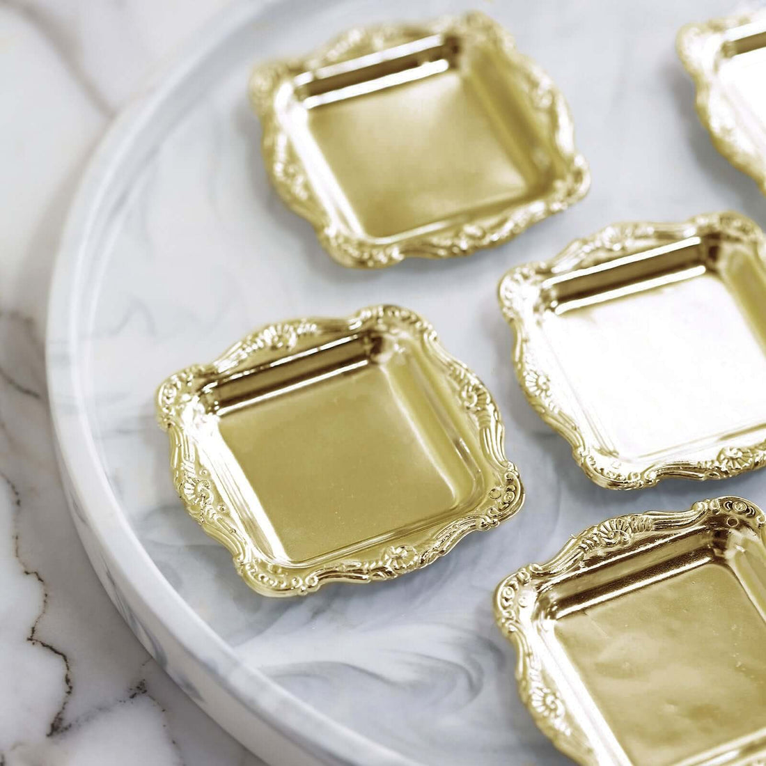 Set of ornate gold square trays on a marble surface.