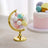Colorful globe candy dispenser with pastel gumballs on a wooden surface.