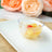 Fruit cocktail in a clear bowl on a white plate, with pink flowers in the background.