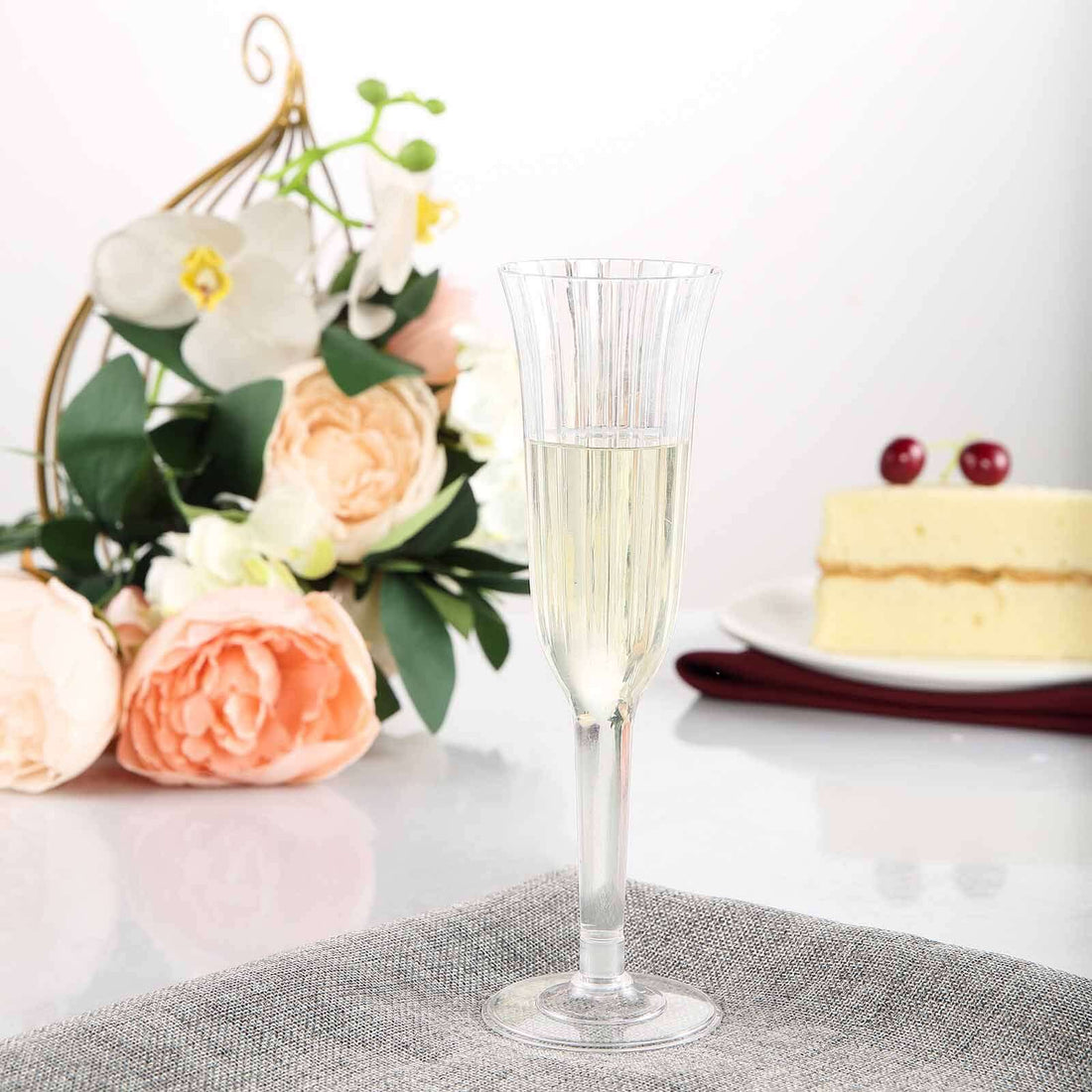 Elegant champagne flute with sparkling drink, surrounded by flowers and cake.